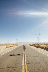 Rear view of woman walking on road by desert during sunny day - CAVF46378