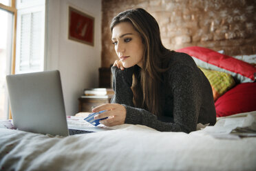 Frau beim Online-Shopping auf dem Laptop, während sie zu Hause auf dem Bett liegt - CAVF46400