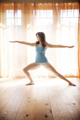 Frau macht Yoga gegen das Fenster zu Hause an einem sonnigen Tag - CAVF46404