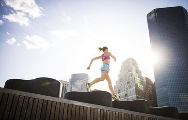 Low angle view of woman running on retaining wall against buildings in city - CAVF46428