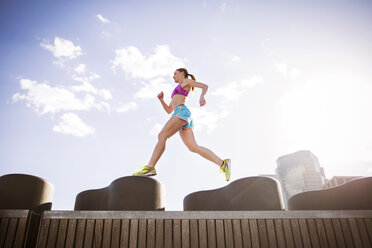 Low angle view of woman running on retaining wall against buildings in city - CAVF46429