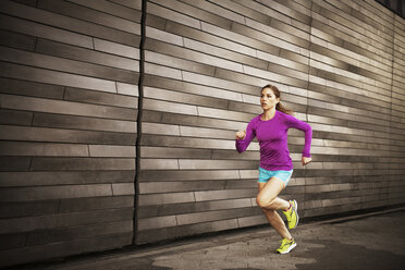 Frau joggt auf dem Gehweg an der Mauer - CAVF46441