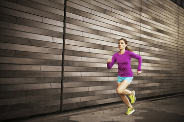 Woman jogging on sidewalk by wall - CAVF46441