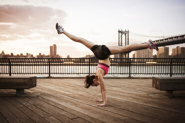 Woman doing splits on handstand at promenade against Manhattan bridge - CAVF46453