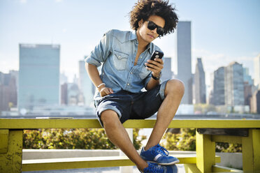 Young man using phone while sitting on bench - CAVF46466