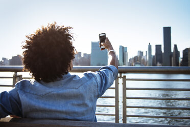 Young man using phone while sitting on bench against city - CAVF46470