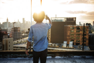 Junger Mann fotografiert Stadt gegen Himmel bei Sonnenuntergang - CAVF46478