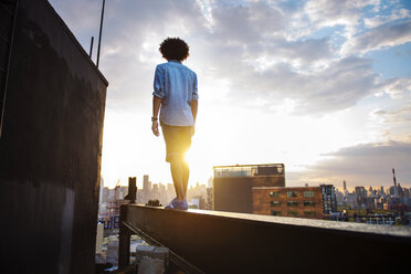 Young man standing on metal against sky during sunset - CAVF46482