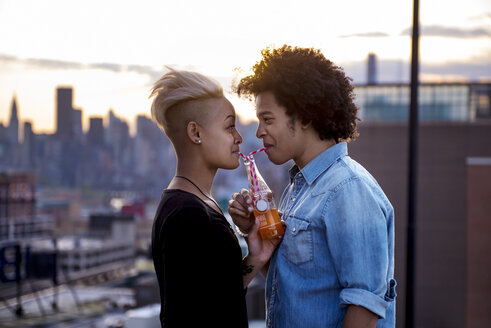 Paar trinkt bei Sonnenuntergang auf dem Dach aus einer Flasche - CAVF46487