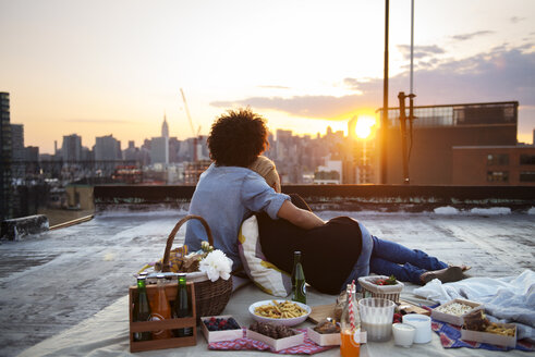 Ehepaar entspannt sich beim Picknick auf dem Dach gegen den Himmel - CAVF46492
