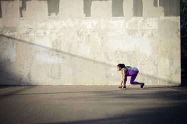 Frau in Startposition auf der Straße, bereit, gegen die Wand zu laufen - CAVF46497