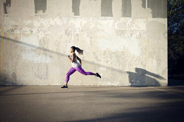 Frau joggt auf der Straße an der Mauer - CAVF46498