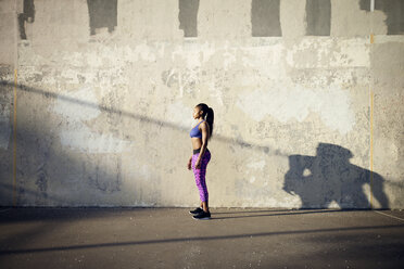Seitenansicht einer auf der Straße stehenden Sportlerin an einer Mauer - CAVF46502