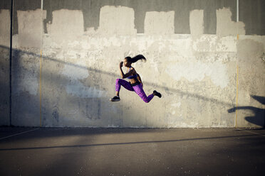 Seitenansicht einer Sportlerin, die in der Luft gegen eine Wand springt - CAVF46504