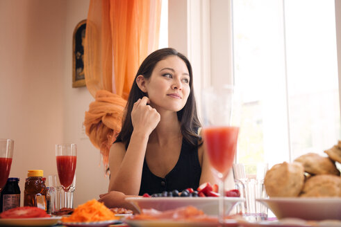 Lächelnde Frau beim Essen, während sie zu Hause sitzt - CAVF46530