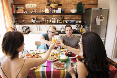 Freunde stoßen mit einem Getränk an, während sie eine Mahlzeit zu Hause genießen - CAVF46541