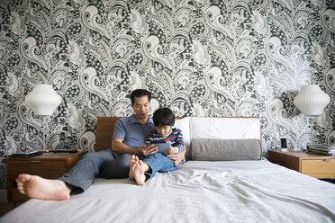Vater und Sohn benutzen ein Tablet, während sie zu Hause im Bett liegen - CAVF46579