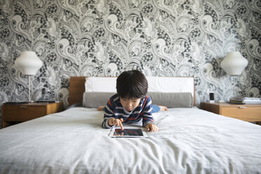 Boy lying on bed and using digital tablet in bedroom - CAVF46580