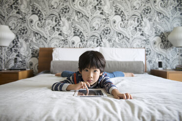 Portrait of boy lying on bed and using digital tablet - CAVF46581