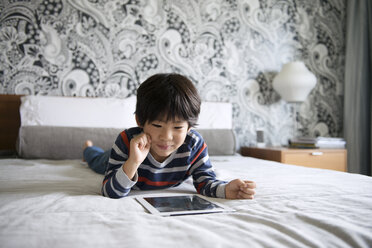 Happy boy using digital tablet while lying on bed - CAVF46582