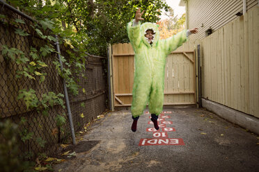Porträt eines Jungen in einem Kostüm, der im Hinterhof hüpfend spielt - CAVF46593