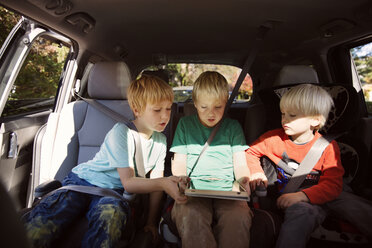 Brüder schauen auf einen Tablet-Computer, während sie im Auto sitzen - CAVF46601
