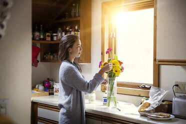Seitenansicht einer Frau, die Blumen in einer Vase auf dem Küchentisch arrangiert - CAVF46611