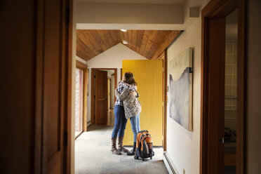 Tochter und Mutter umarmen sich in voller Länge an der Tür eines Hauses - CAVF46620
