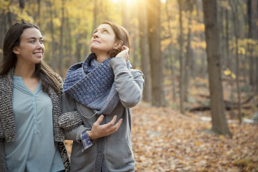 Happy daughter and mother walking amidst trees in forest - CAVF46622