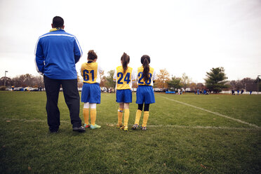 Rear view of soccer players standing with coach on playing field - CAVF46642