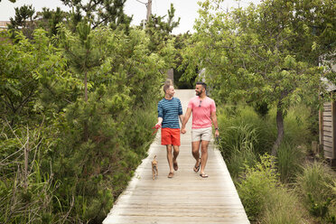 Glückliches homosexuelles Paar im Gespräch beim Spaziergang mit Chihuahua auf der Promenade - CAVF46654