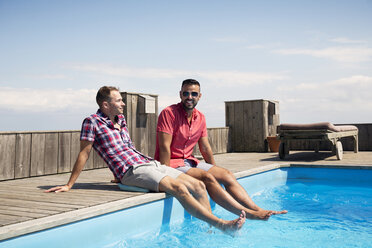 Homosexual couple resting on poolside against sky - CAVF46668
