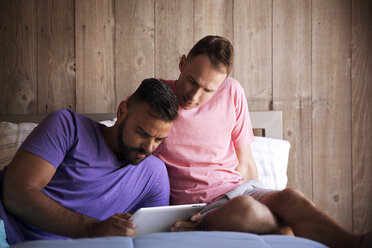 Homosexual couple using tablet computer while lying on bed at resort - CAVF46673
