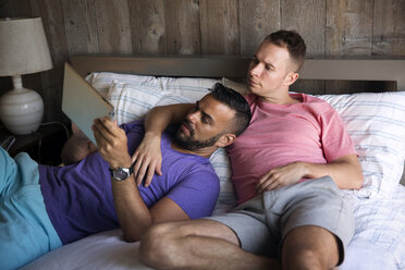 Homosexuelles Paar schaut auf Tablet-Computer, während sie auf dem Bett in einem Resort liegen - CAVF46674
