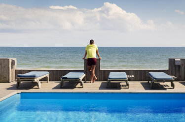 Rückansicht eines schwulen Mannes, der am Pool steht und das Meer gegen den Himmel betrachtet - CAVF46678