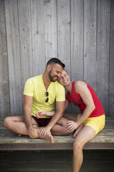 Happy homosexual couple sitting on wooden bench at resort - CAVF46682