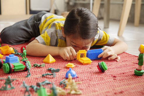 Mädchen spielt mit Spielzeug, während sie zu Hause auf dem Boden liegt - CAVF46698