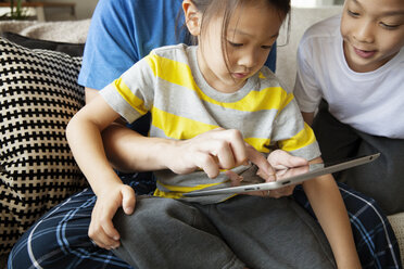 Mittelteil eines Vaters, der seine Tochter bei der Benutzung eines Tablet-Computers anleitet, während er mit seinem Sohn auf dem Sofa sitzt - CAVF46703