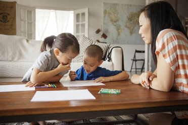 Mother looking at children drawing on table in living room - CAVF46709
