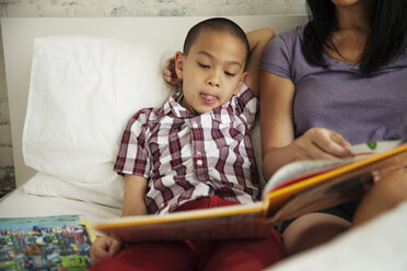 Junge hört seiner Mutter zu, die zu Hause auf dem Bett ein Buch liest - CAVF46715