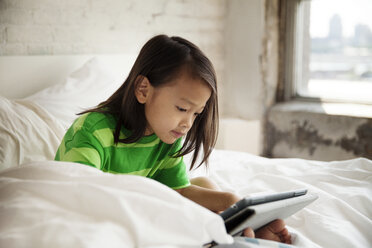 Smiling girl using tablet computer while resting on bed at home - CAVF46717