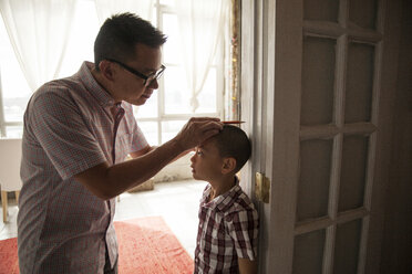 Vater misst die Größe seines Sohnes, während er an der Tür eines Hauses steht - CAVF46727