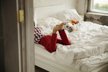 Boy lying on bed seen through doorway at home - CAVF46731