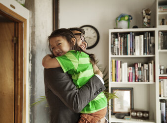 Glücklicher Vater, der seine Tochter umarmt, während er zu Hause im Wohnzimmer steht - CAVF46732