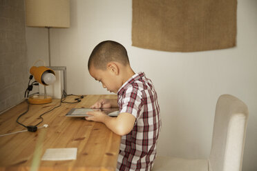 Seitenansicht eines Jungen, der am Tisch an der Wand einen Tablet-Computer benutzt - CAVF46736