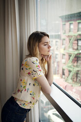 Thoughtful woman looking through window while standing at home - CAVF46746