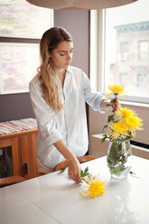 Junge Frau dekoriert Vase mit Chrysanthemen zu Hause - CAVF46763