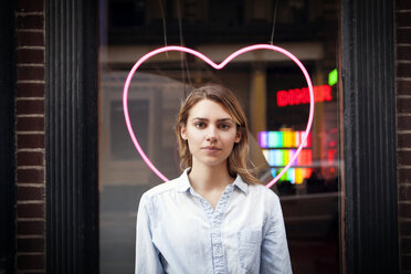 Portrait of woman standing against illuminated heart shape decoration at shop - CAVF46768