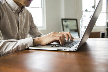 Mittelteil eines Geschäftsmannes, der einen Laptop am Tisch in einem kreativen Büro benutzt - CAVF46802