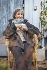 Porträt einer lächelnden Frau, die mit einer Kaffeetasse in der Hand sitzt und in die Kamera schaut - MASF06839
